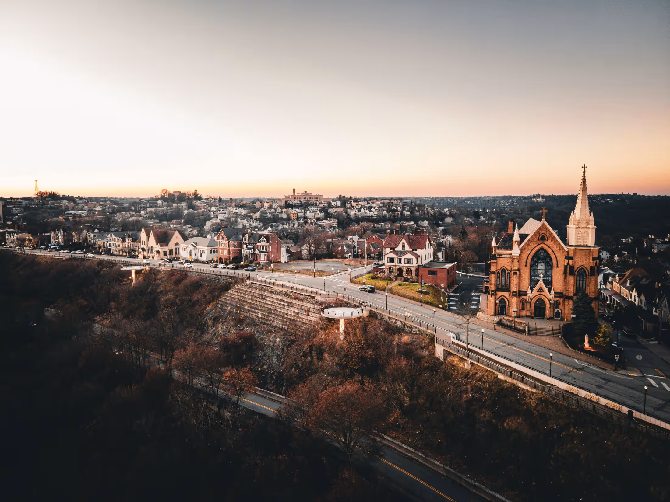 Aerial view of a Pittsburgh hillside neighborhood at dusk, rows of houses and street trees